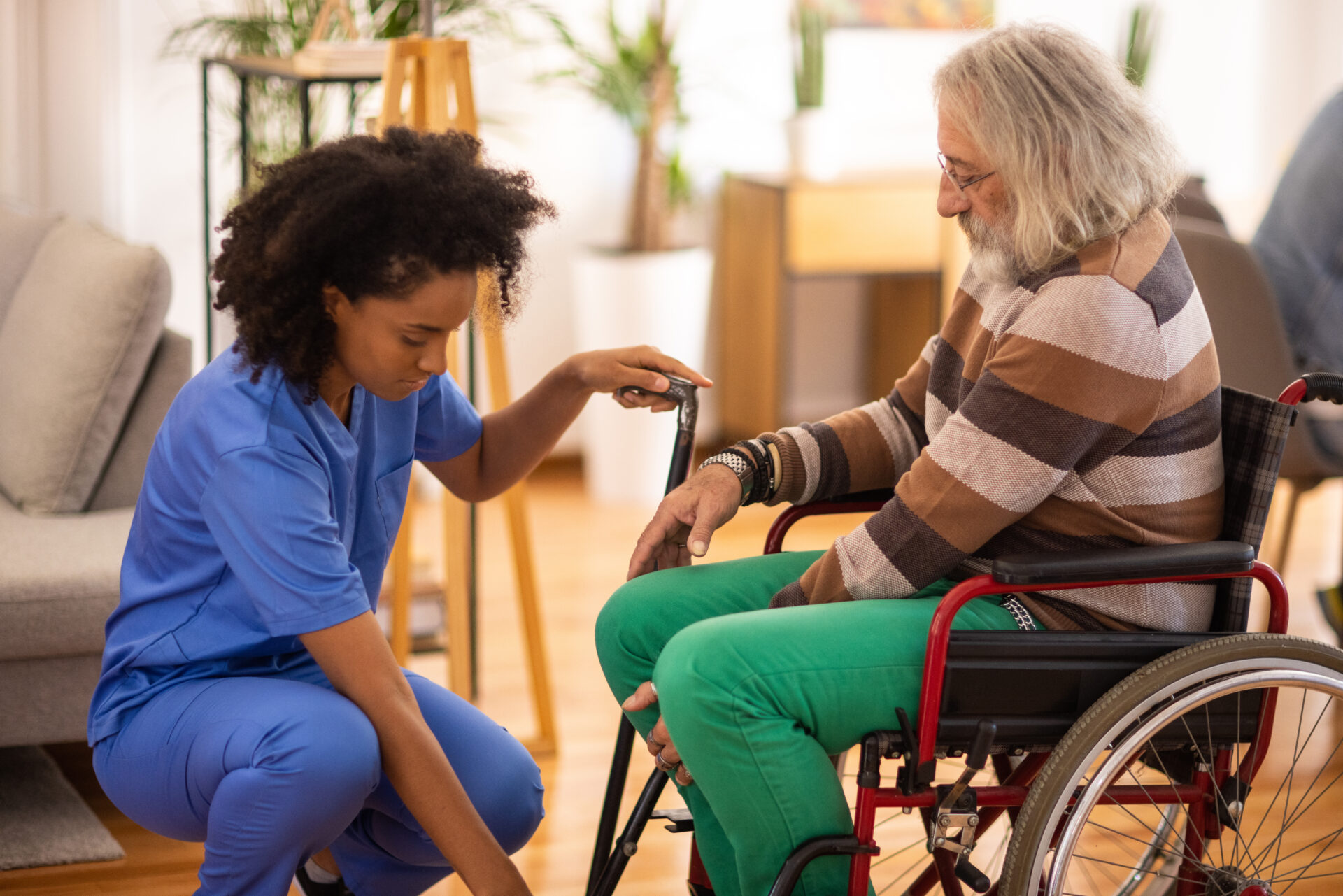 Female nurse helping senior man to get up from wheelchair in nursing home